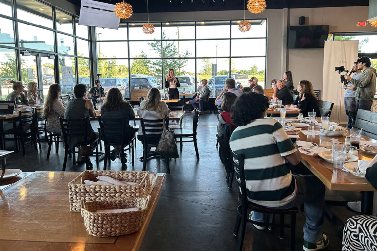a woman standing in front of a group of people sitting at a table