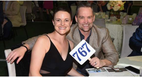 A couple at a charity gala table holding up bid paddle number 767