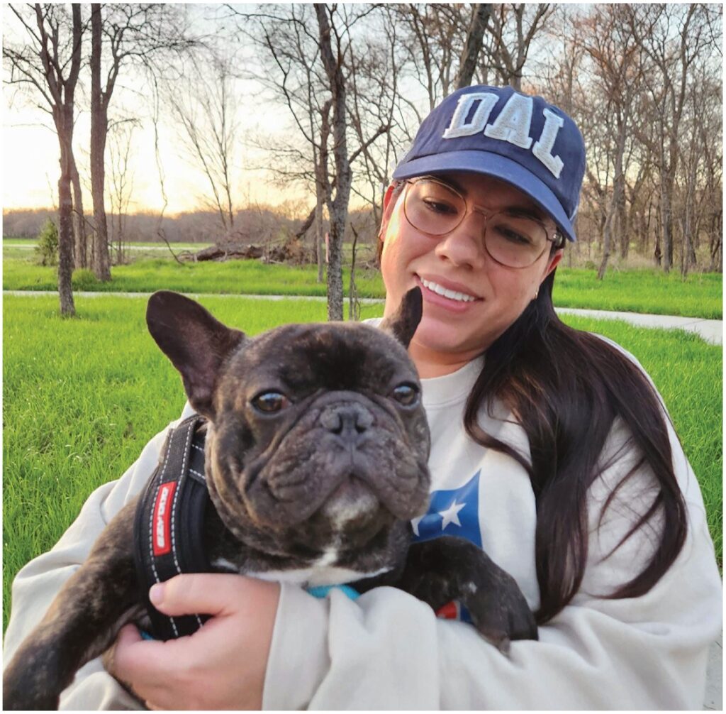 A woman in a Dallas cap holding a French bulldog outdoors