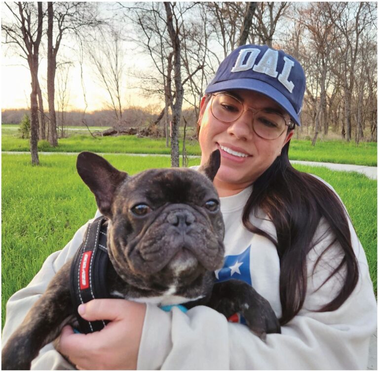 A woman in a Dallas cap holding a French bulldog outdoors