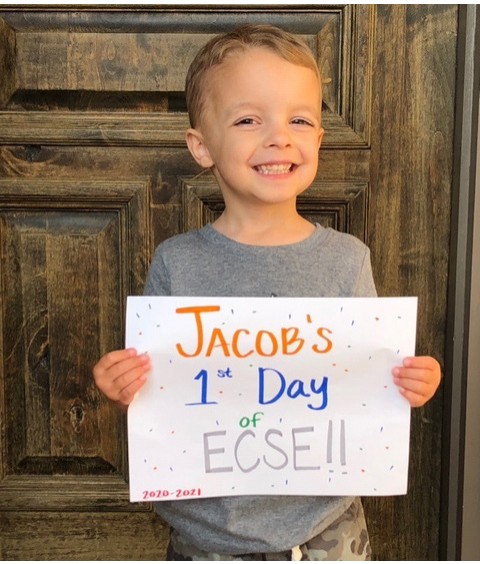 A young boy holding a sign that reads Jacob's 1st Day of ECSE