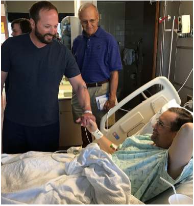 Two men standing beside a patient in a hospital bed