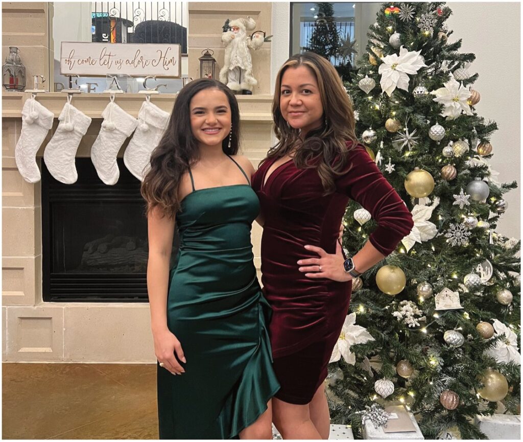 Two women posing by a fireplace and a decorated Christmas tree