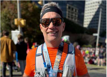 A runner in sunglasses and a hydration vest smiling at a race