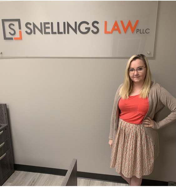 A woman standing in the Snellings Law office beneath the firm's sign