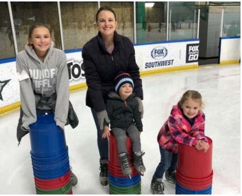 A mother and her three children ice skating with skating aids at a rink