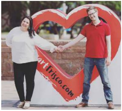 Two people holding hands in front of the heart-shaped Art Frisco sign