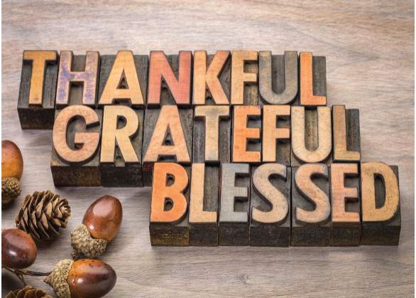 Wooden letterpress blocks spelling Thankful, Grateful, Blessed beside acorns and pine cones