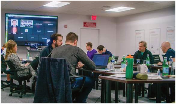 Business owners seated at tables during a mastermind meeting, with a video call on the screen
