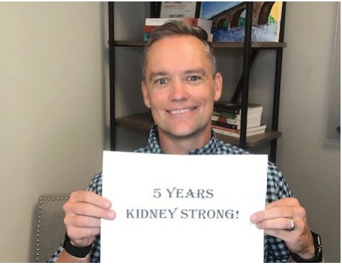 A man holding a sign that reads 5 Years Kidney Strong!