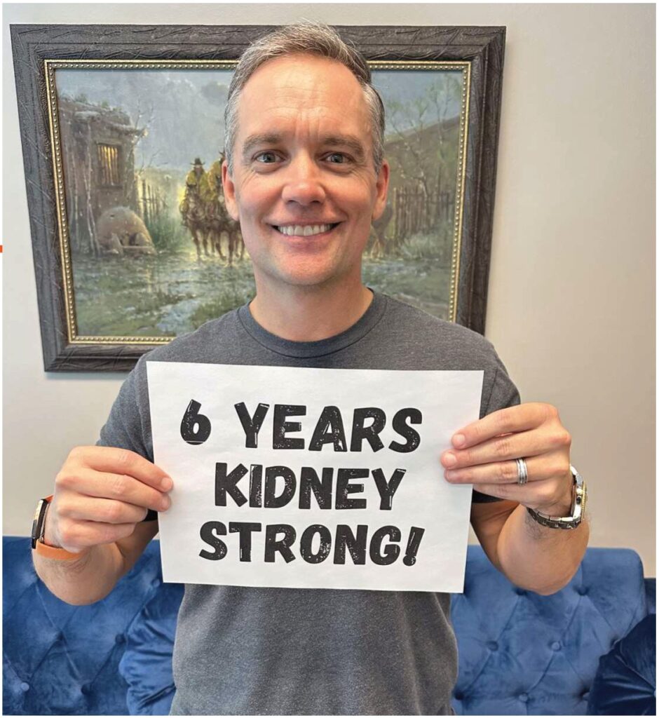 A man holding a sign that reads 6 Years Kidney Strong!